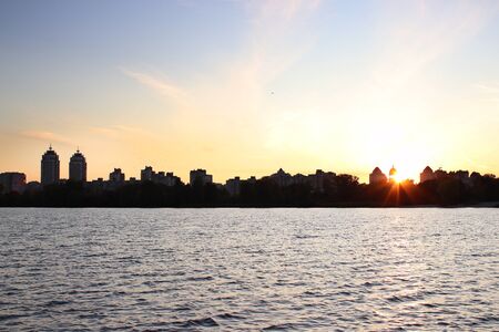 Wonderful sunset on the river or lake. On the horizon are silhouettes of trees and beautiful city buildings. Calming atmosphereの写真素材