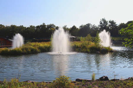 Artificial lake with fountains in a beautiful landscape park. Lush greenery. Hot sunny day. Summerの写真素材