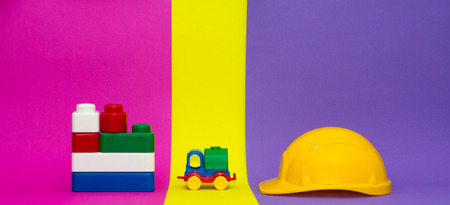 Color truck, yellow safety helmet and color blocks isolated on multicolor background. Building construction concept or project construction backgroundの写真素材