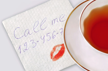 Cup of tea and napkin with a text "Call me", a phone number and a kiss.の写真素材