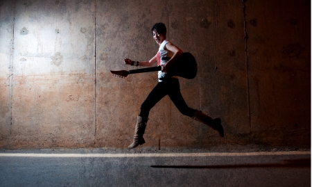 dark grunge style asian rock star jumping and holding a guitarの写真素材