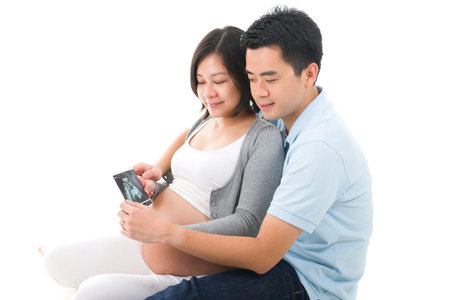 Young asian pregnant couple expecting a child holding ultrasound