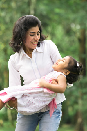 indian mother carrying daughter playing in outdoor parkの写真素材