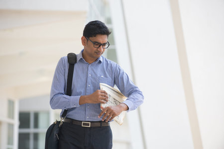 Indian man checking on new office to let, holding newspaper and calling on phone.の写真素材
