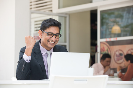 young indian business male on laptop and coffee at a cafe with happy emotionの写真素材