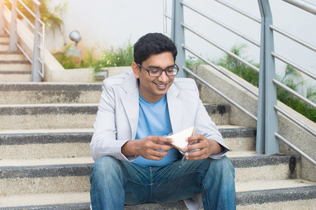 indian male eating a quick sandwich outdoor in casualの写真素材