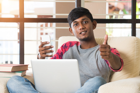 teenage indian male using laptop and phone thumbs upの写真素材