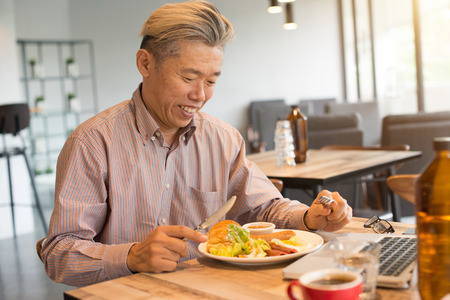 matured asian business male having breakfastの写真素材