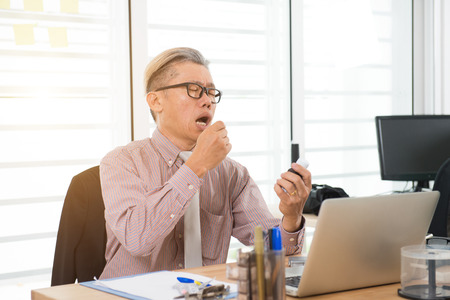 asian senior business man taking medicine at workの写真素材