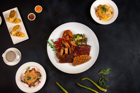Gourmet cooked meats and vegetables in frying pans with seasoning and garnishes on a dark  with copy...