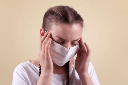 Girl in a medical mask. Girl on a yellow background. The girl is holding on to her temples, she looks tired, sickly. The girl is protecting herself from infection.の写真素材