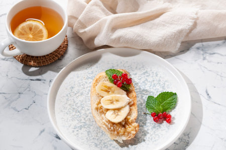 Appetizer sandwich with banana, red currant and mint greens. Tea with lemon.の写真素材