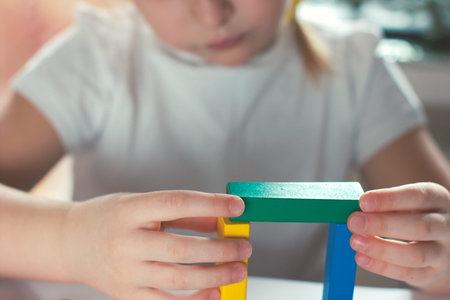 little blond girl playing board games. wooden builing blocks in girls hands.