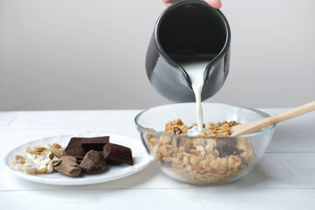 homemade granola with chocolate and nuts. granola in a transparent bowl with pouring milk and chocolate on a plate. cashews and raw cocoa pieces. organic breakfast concept.の写真素材