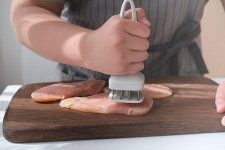 chef using tenderizer for fresh chicken steaks. tenderised chicken breasts on cutting board. spicy...