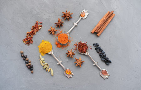 Top view of mix bright spices in vintage silver spoons as ingredient for tasty meal on gray concrete...
