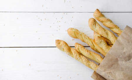 Italian grissini or salted breadsticks. sesame breadsticks in a craft paper on white wooden table....