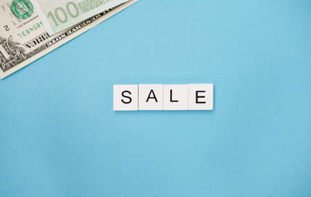 The Word Sale are spelled out in wooden letter tiles and banknotes on a blue trendy background. promotion seasonal offer ads.の写真素材