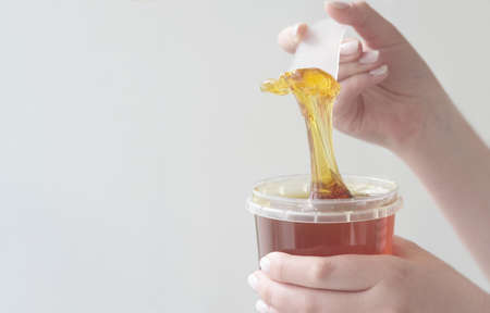 sugar paste or wax honey for hair removing flows down from waxing spatula stick. beauty spa concept. sugaring depilation.の写真素材