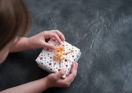 little girl looking at gift box with orange bright stars and bow. children gifts and surprise...