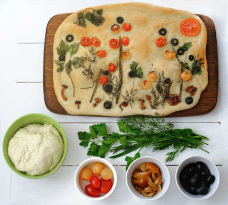 focaccia gardens trend. focaccia bread with ingredients on white wooden table. social media trendy food. Traditional Italian bread with tomatoes, black olives and greens. baked flat breadの写真素材