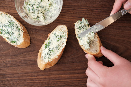 human hands spreading herb butter on a baguette. healthy butter with dill and cilantro on a bread...