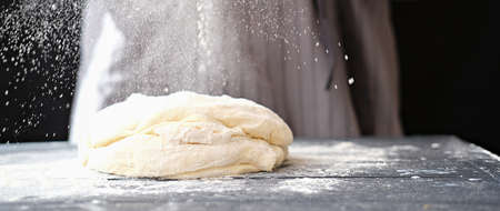 dough for bread or pizza. bakery or homemade bread in process, dough with flour powder against black background. Concept of baking and patisserie.の写真素材