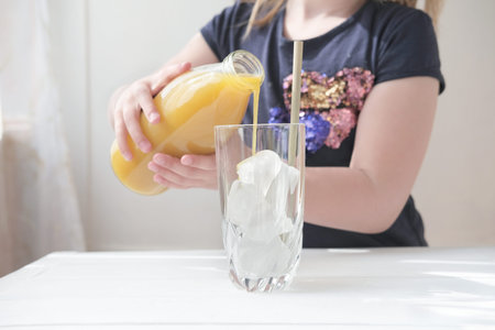 little girl pouring mango juice in a glass. iced frothy drink. tropical flavored juice. ice cubes in a glass. cold drinks for summer time.の写真素材