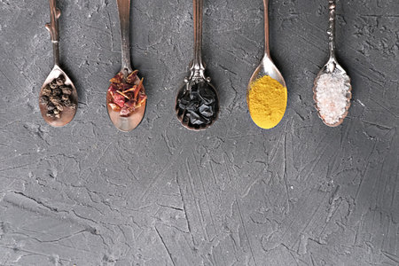 Colorful various spices for cooking in spoons on dark background. curcuma powder, juniper berries,...