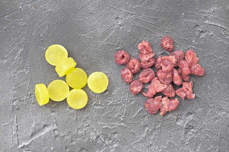 yellow candies compare to dried cranberries on gray background. sugar substitution concept. eating healthy berries not sugal. less sugar consumption.の写真素材