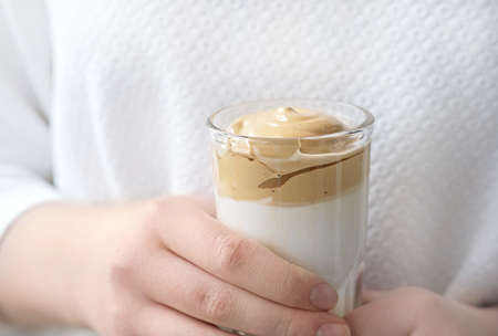 Iced frothy Dalgona Coffee, a trendy fluffy creamy whipped coffee. Korean drink latte espresso with coffee foam. girl holding cup with instant coffee.の写真素材