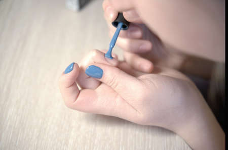 Young woman applying nail polish with brush from bottle, polishing painting fingernails with blue color enamel, doing manicure at home, perfect healthy nails careの写真素材