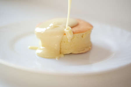 Trendy asian breakfast, Fluffy Japanese souffle pancake, milk sause pouring on hot pancake on a plateの写真素材