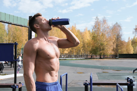 toned muscular man drinking whey protein cocktail after workout. autumn stadium, outdoors aclive...