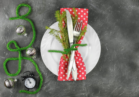 christmas decorated plate and tableware with red napkin and green ribbon. holiday silverware on dark...