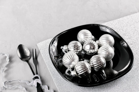 Christmas table setting. Christmas tree balls on a black plate, knife, fork. black dinnerware. The...