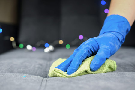 Hand in protective glove cleaning sofa with rag. christmas cleaning or clean up. Maid cleans...