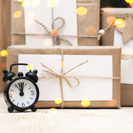 hand made christmas gifts wrapped in craft paper and alarm clock. bokeh lights. christrmas...
