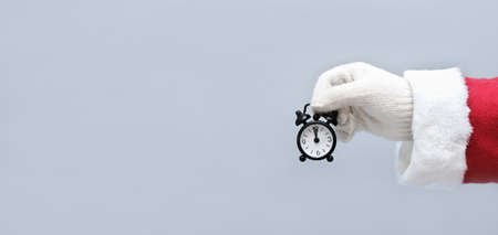 santa holding an alarm clock with 12o'clock time. christmas and new year concept. crop view. banner size. copy space. small black alarm clock in santa's handの写真素材