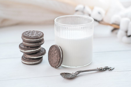 A Stack of chocolate Cookies with Milk in glass. beautiful spoon near a glass. cozy sweater and cotton flowers on a background. good morning concept.の写真素材