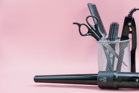 hair stylist tools in a basket. scissors, brush, comb, curling iron. pink background. home hair care. beauty salon tools. hairdresser's equipment. copy spaceの写真素材
