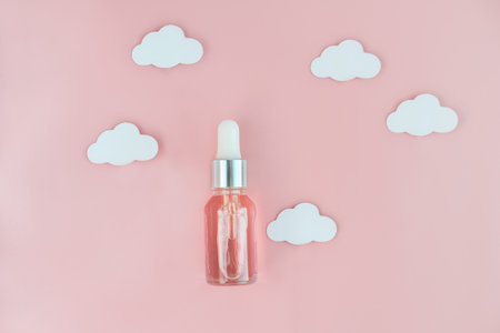 An essential oil. moisturizing treatment. Natural herbal serum in a glass bottle with a pipette. pink background with clouds. Dry skin care. facial skincare product. top view.の写真素材