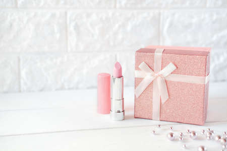 pink lipstick and a gift box on a table. pink necklace. holiday prasent for valentines or birthday. female gift copy space. boxing day concept.の写真素材