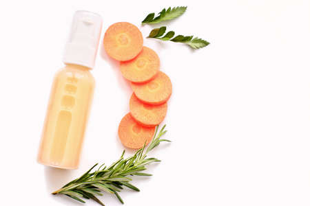 transparent cosmetic bottle with carrot cream or lotion. natural cosmetic ingredients. slices of carrot next to the bottle. home grown cosmetics. copy space. top viewの写真素材