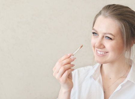 young pretty woman applying concealer on a nose and smiling. perfect skin tone and make up. copy space for text.の写真素材