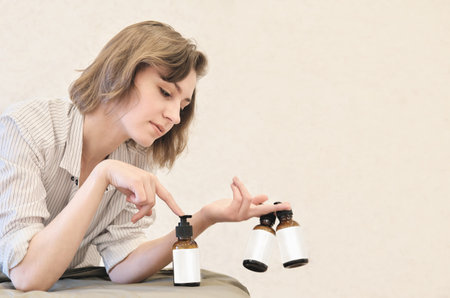 Portrait of a young woman holding bottles with lotion or cream at home. cosmetic unbranded bottles...