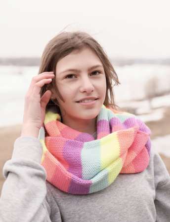 beautiful teenager girl wearing festive multicolored scarf and looking at camera. outdoors walking. happy girl with hair blowing with a wind.の写真素材
