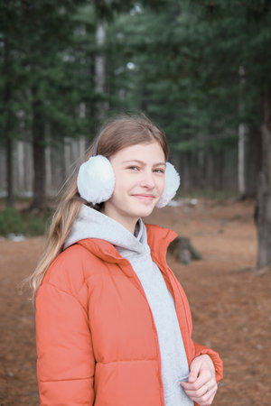 beautiful teenager girl wearing red jacket and earmuffs walking in the park. schoolgirl in the...