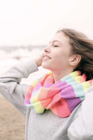 outdoor portrait of a teenager girl wearing striped scarf and enjoying warm wind. smiling happy cheerful girl on a river bank.の写真素材