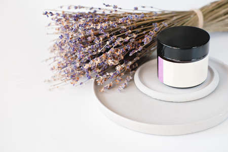 lavender face cream in an unbranded jar on a cement trays with lavender flowers on background. copy space. calming and soothing ingredient for aromatherapy and beauty care.の写真素材